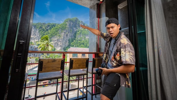 A man standing on a balcony with a view of a mountain and palm trees. - Sleeper Hostel (Krabi)