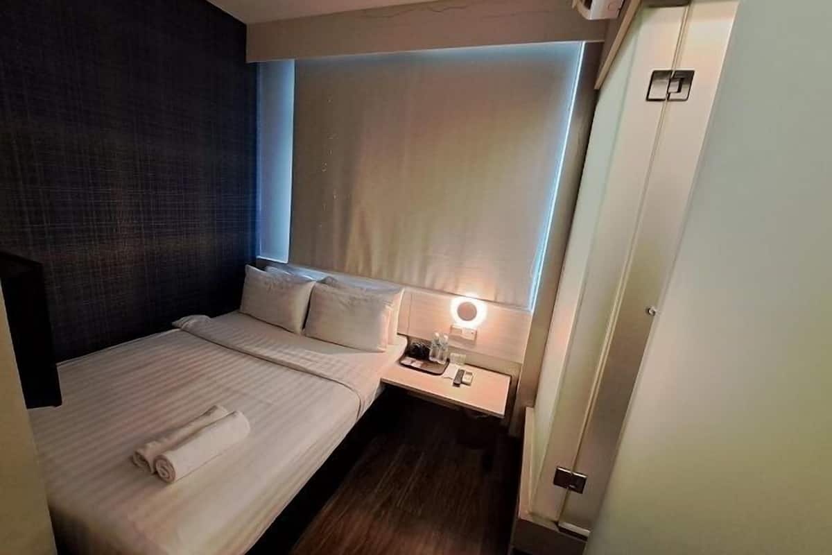 A hotel room with a bed, a bedside table, a nightstand, and a window with curtains.
