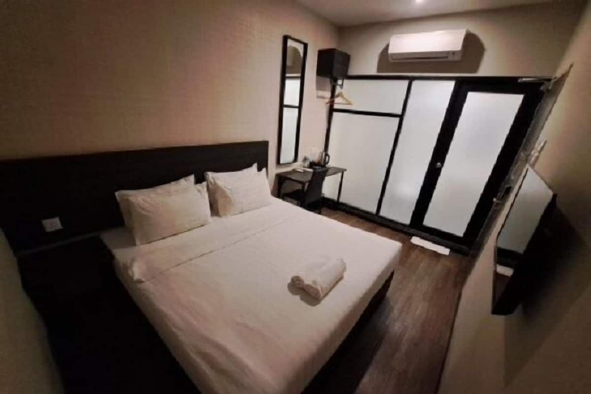 A hotel room with a bed, a bedside table, a lamp, and an air conditioning unit.