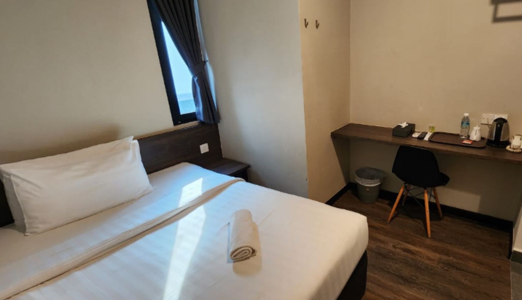 Una habitación de hotel con cama, escritorio, silla y ventana con cortinas.