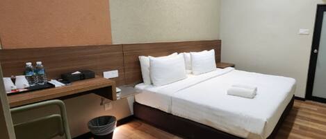Habitación de hotel con cama, escritorio, silla, cubo de basura y unidad de aire acondicionado instalada en la pared.