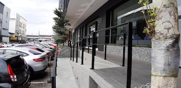 A modern hotel with a covered outdoor area, a parking lot with several cars, and a tree wrapped in protective material.
