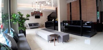 A modern hotel lobby with a grey sofa, a small round table, and a large potted plant.