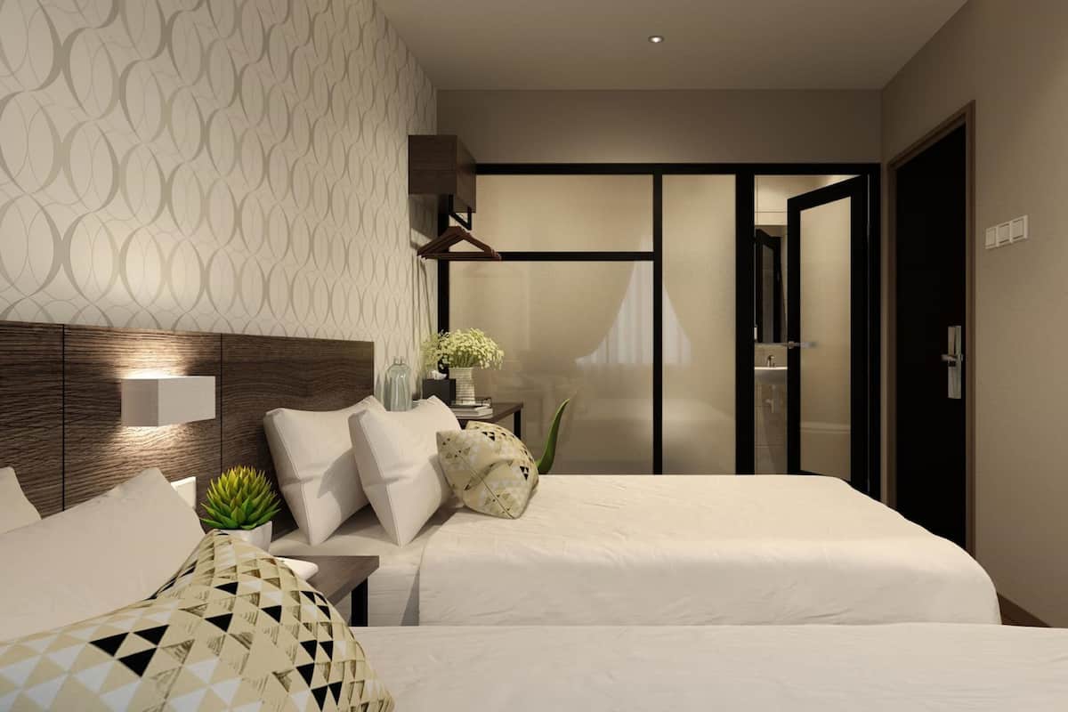 A modern hotel room with two beds, a large TV, and a bathroom visible through a sliding door.