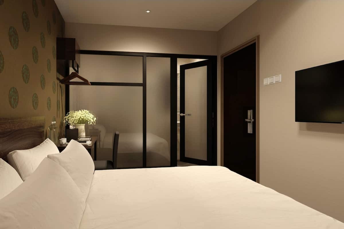 A hotel room with a large bed, a bedside table with a vase of flowers, a chair, and a sliding door leading to another room.