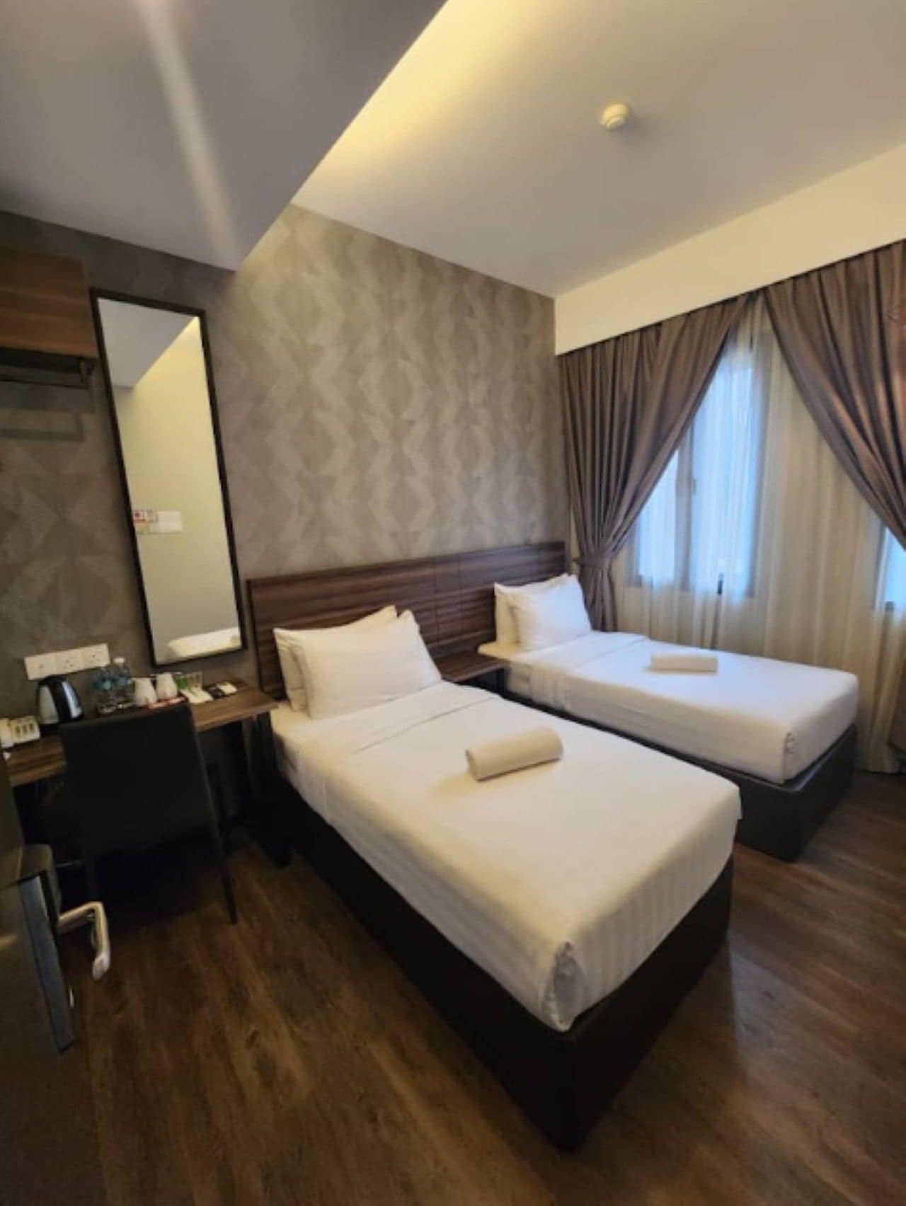 A hotel room with two beds, a desk, a chair, and a mirror.