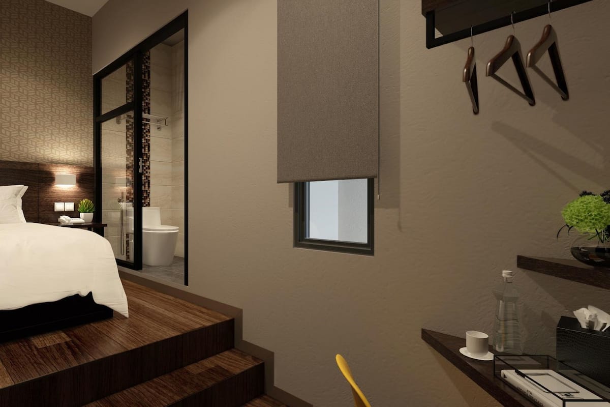 A modern hotel room with a large bed, a shower area, a small window, and a desk with a cup and tissues.