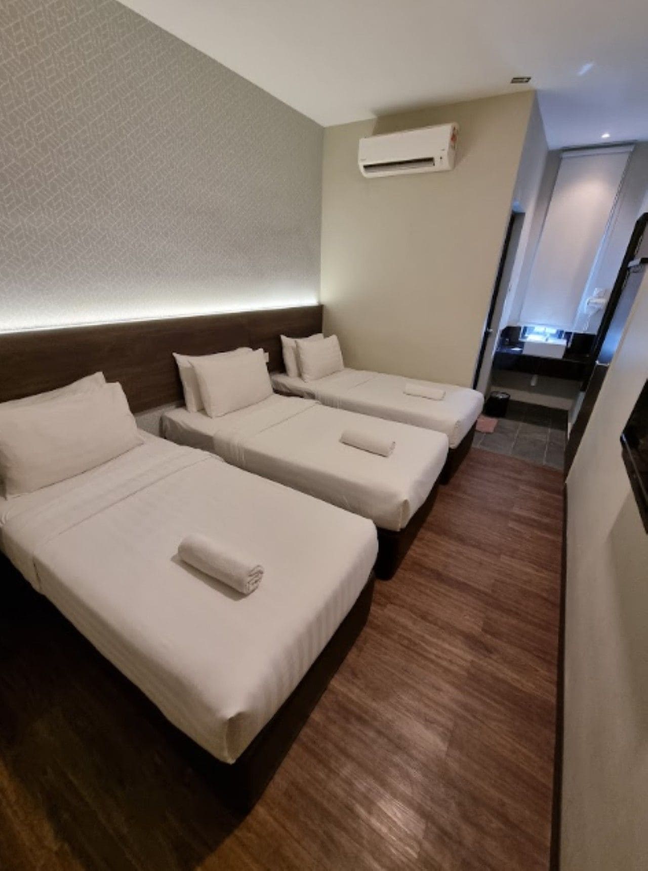 Ein Hotelzimmer mit drei Einzelbetten, Holzboden, Wand-Klimaanlage und einer kleinen Küchenzeile.