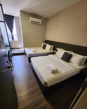 Une chambre d’hôtel avec deux lits, un bureau en bois foncé, un appareil de climatisation et une fenêtre avec des rideaux.