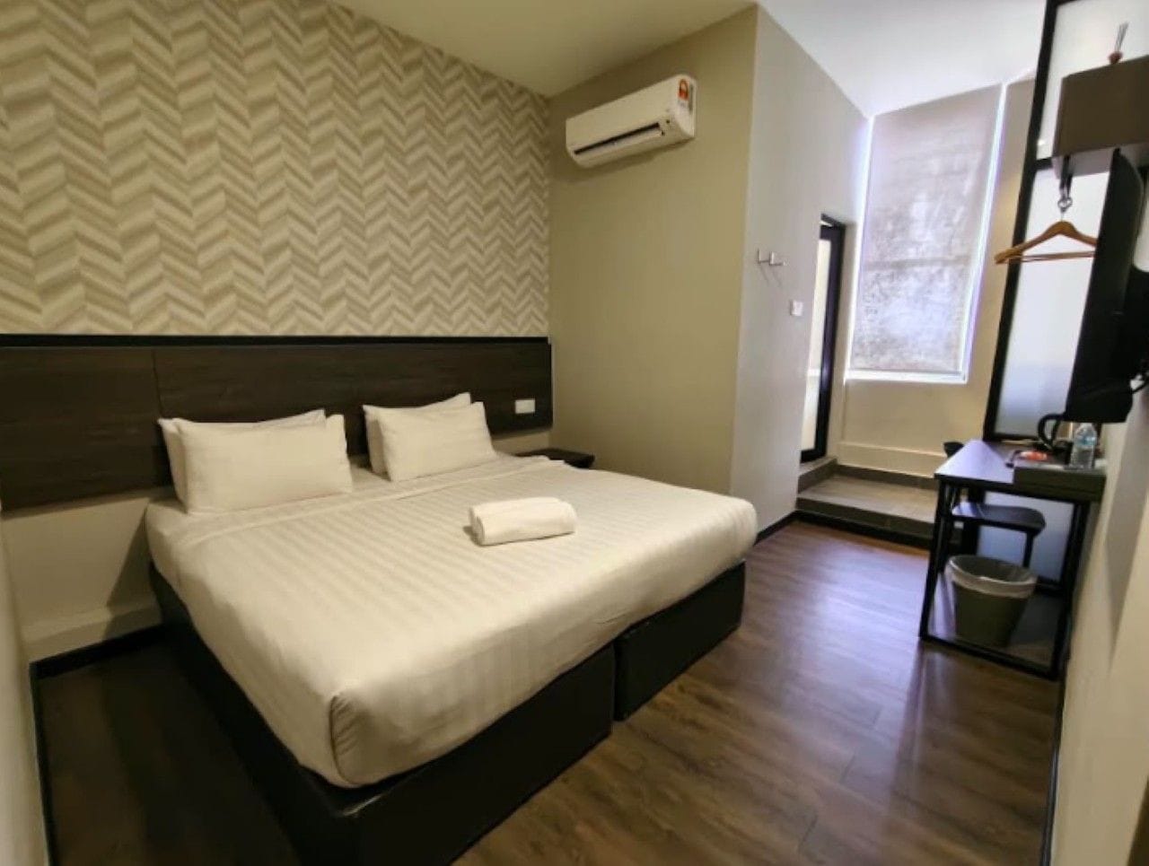 Habitación de hotel con cama, mesita de noche, espejo, equipo de aire acondicionado y ventana.