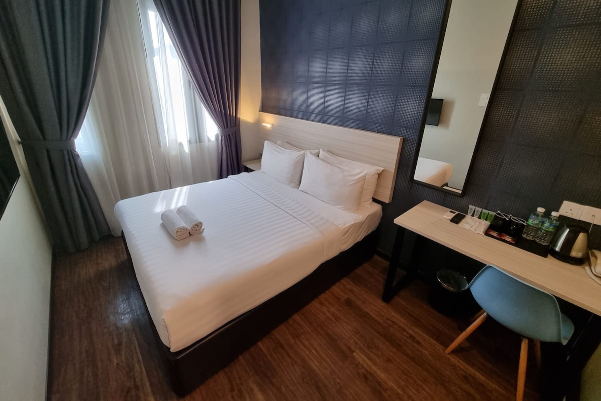 A hotel room with a bed, a desk, a chair, a mirror, and a window with curtains.