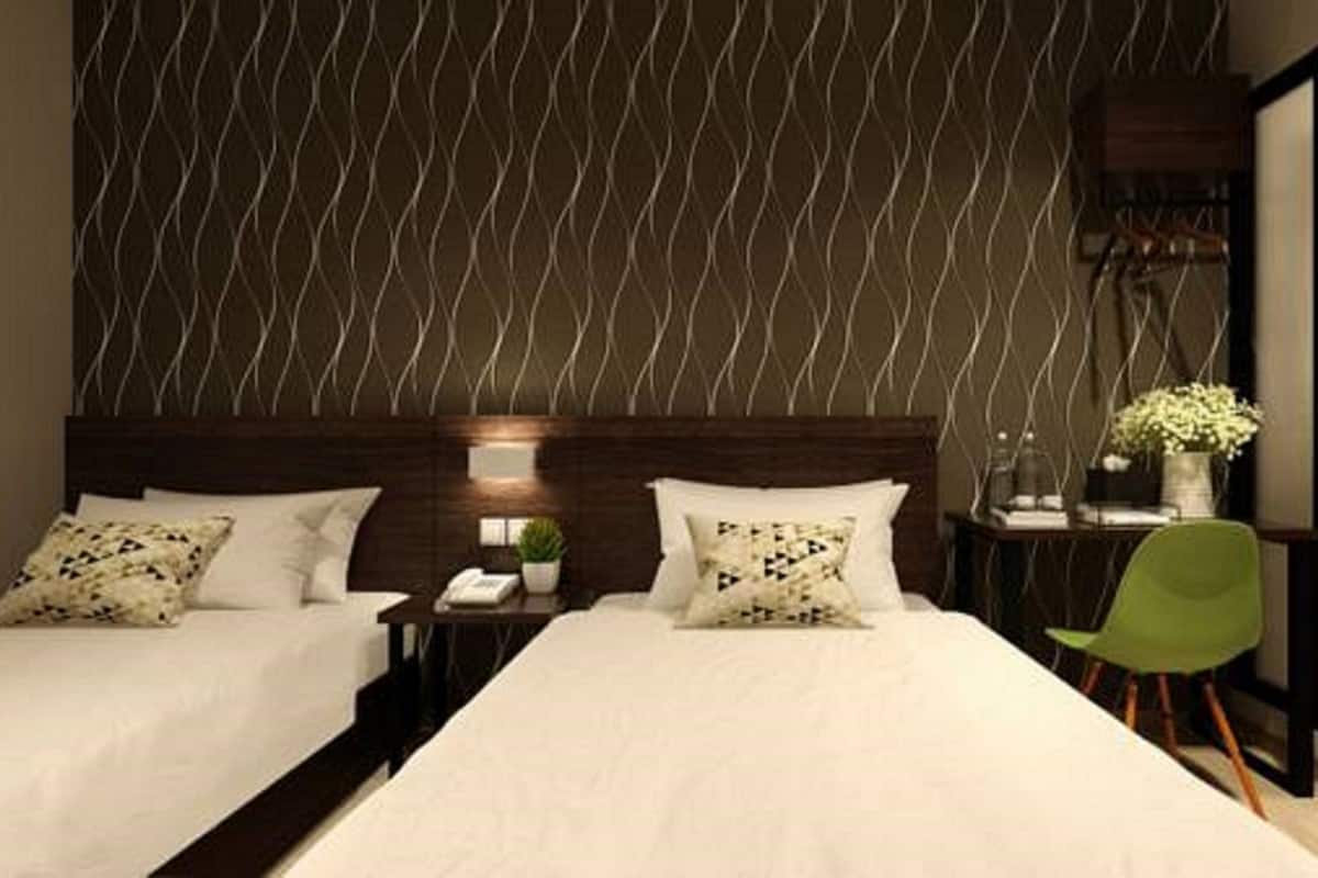 A modern hotel room with two beds, a nightstand, a green chair, and a bathroom with a sink and mirror.