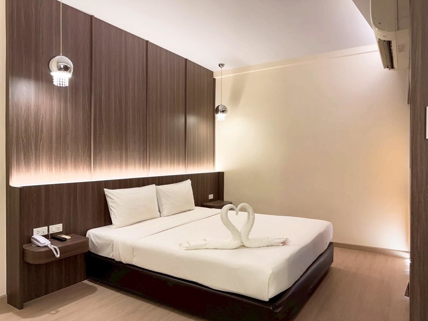 A modern hotel room with a large bed, a bedside table with a phone, and a wall-mounted light fixture.