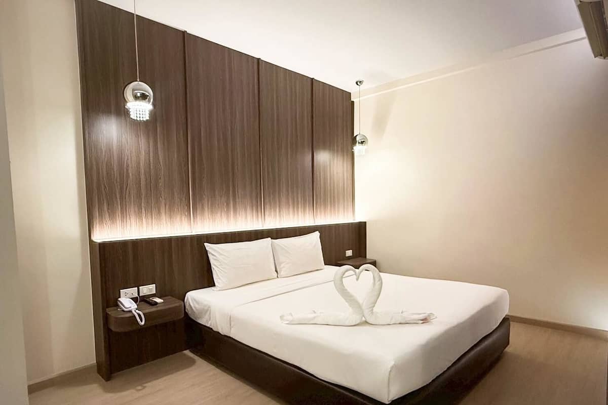 Quarto de hotel moderno com uma cama grande, cabeceira de madeira, mesa de cabeceira com telefone e arranjo de toalhas em formato de coração.