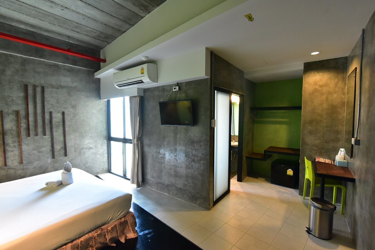 A hotel room with a bed, a TV, a window, and a bathroom.