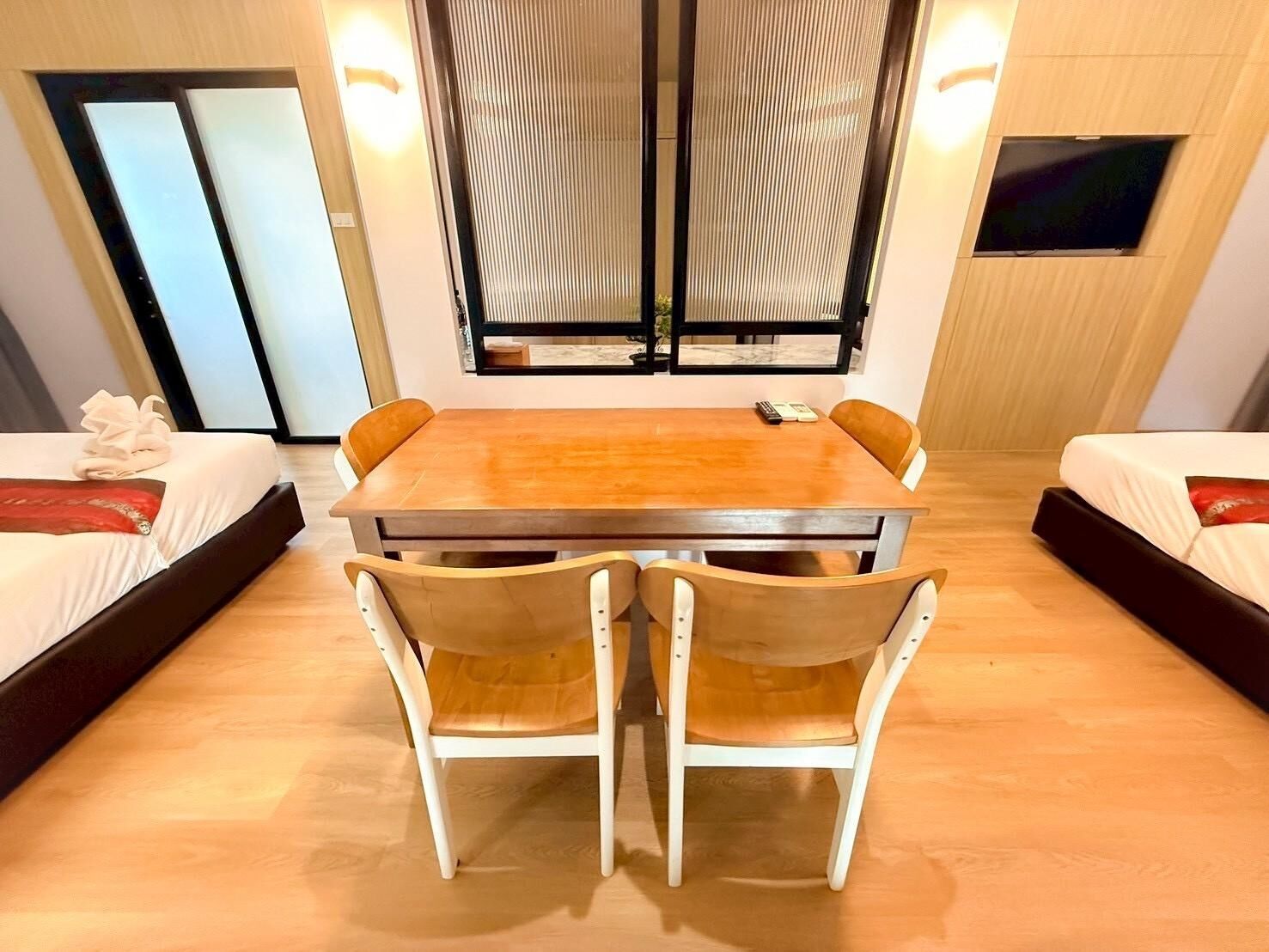 A hotel room with a wooden dining table, four chairs, two beds, and a large window with blinds.