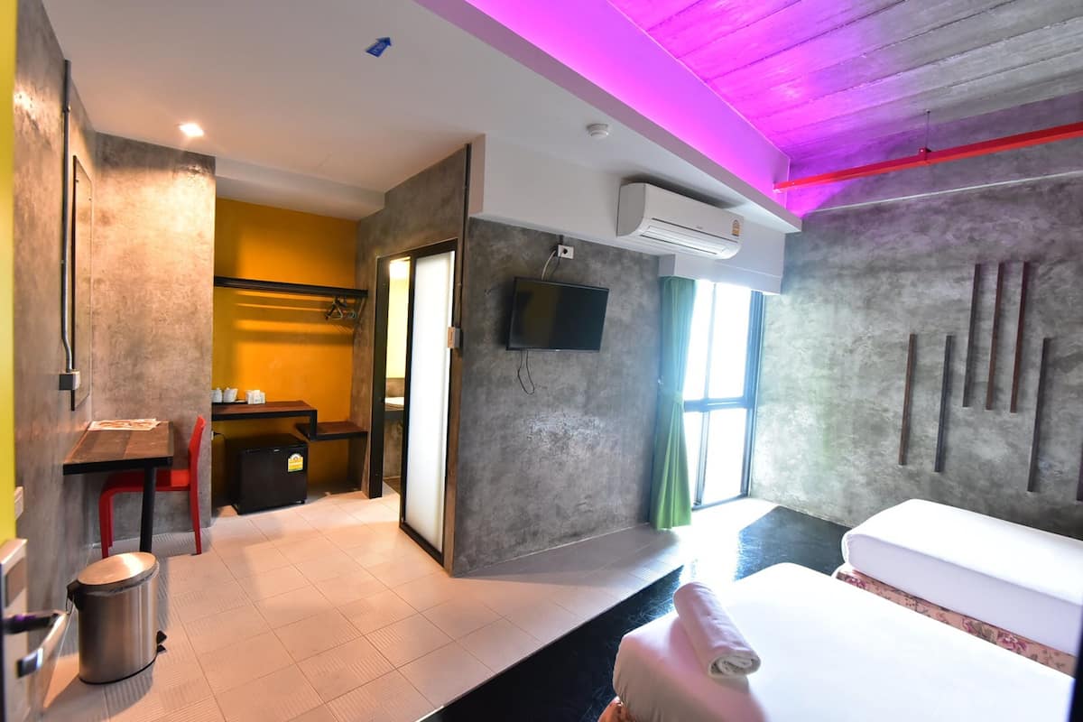 Quarto de hotel moderno com televisão de tela plana, uma cama, uma mesa e uma lixeira.
