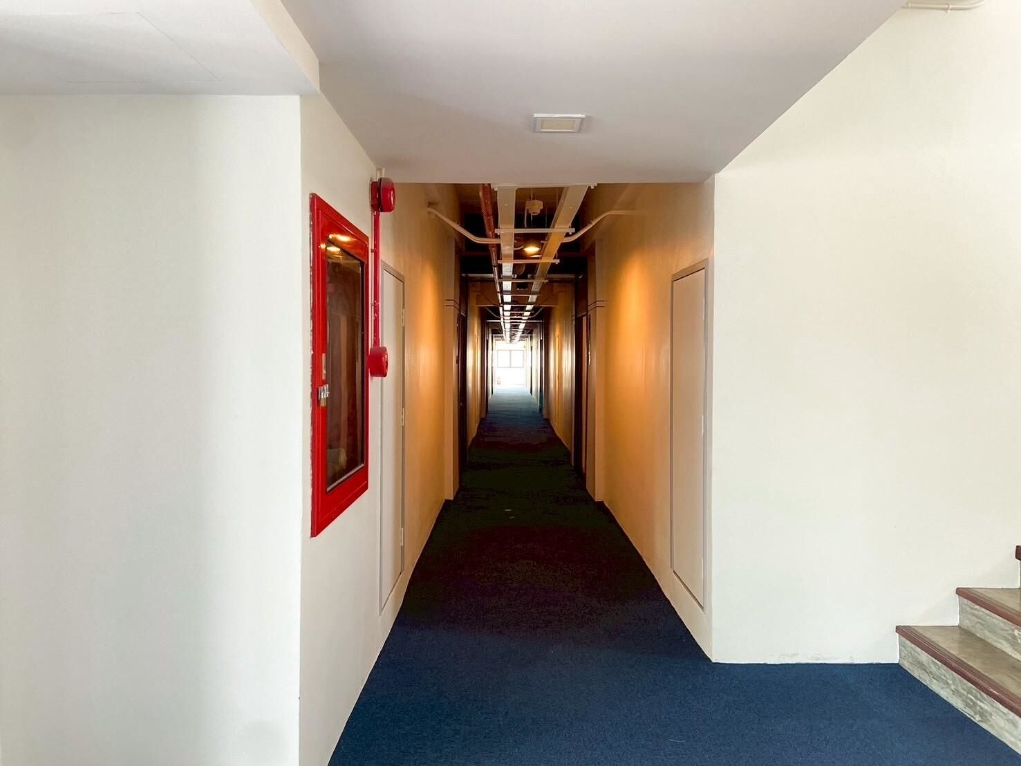 A long, narrow hallway with a blue carpet, white walls, and red-framed doors.