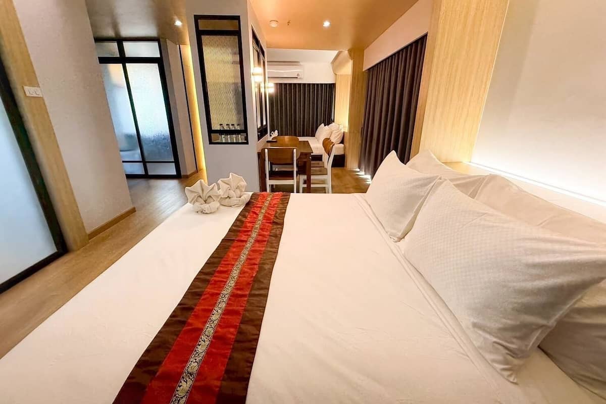 Quarto de hotel com uma cama grande, uma mesa e uma cadeira. Há uma janela com cortinas e vista para o exterior.