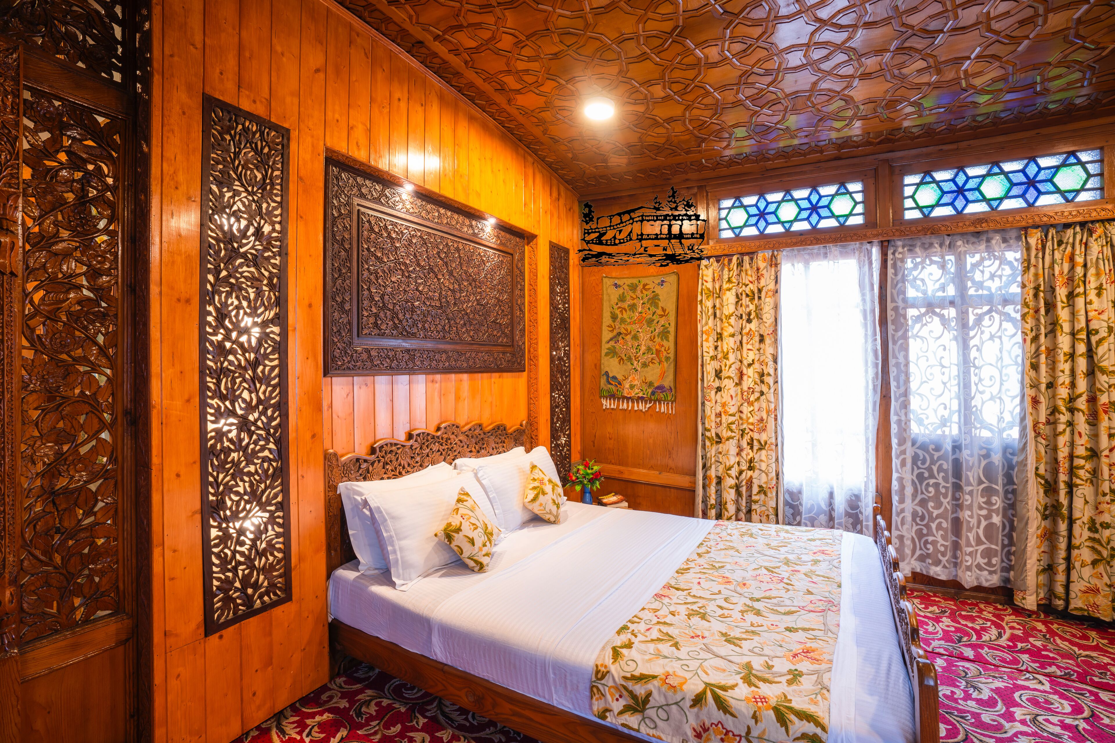 A wooden-paneled room with a bed, floral curtains, and a stained glass window.
