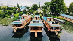 Varias casas flotantes de madera con un letrero que dice "New Jacqueline Heritage" amarradas en un río tranquilo, rodeadas de vegetación y otros edificios.