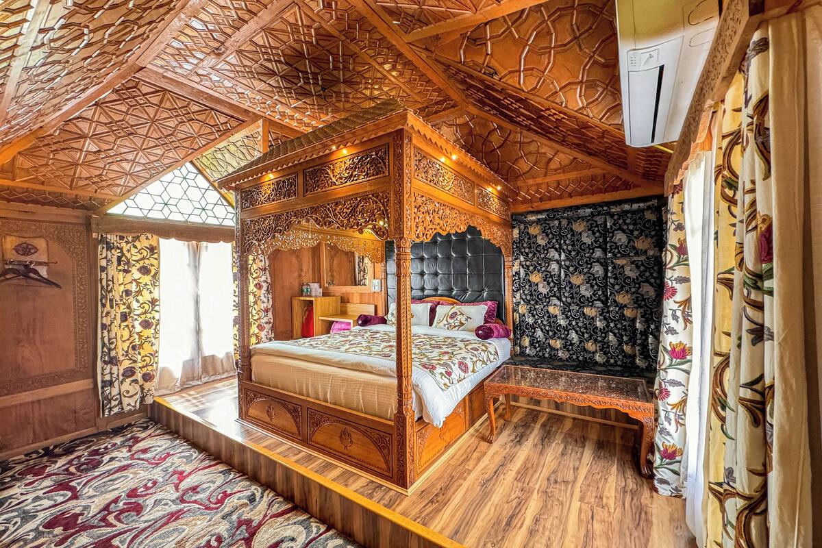 Uma cama com dossel e esculturas detalhadas, piso de madeira e um tapete estampado.
