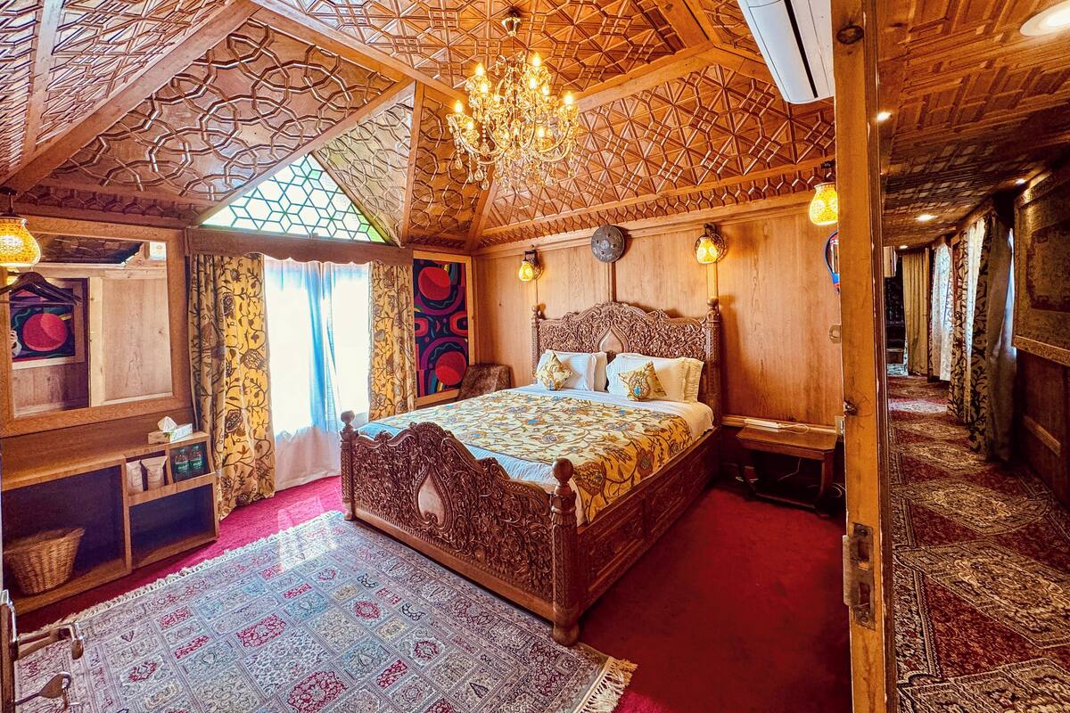 Quarto tradicional com uma cama grande e elaborada, um candelabro e um tapete estampado.