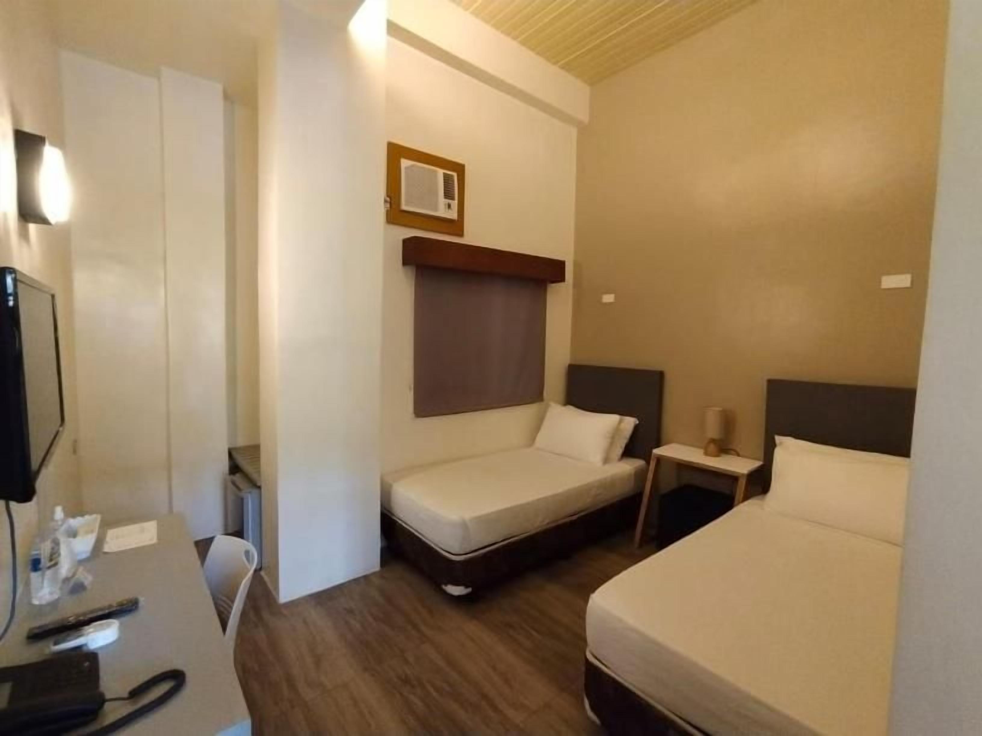 Een hotelkamer met een bureau, twee eenpersoonsbedden, een klein nachtkastje en een televisie aan de muur.