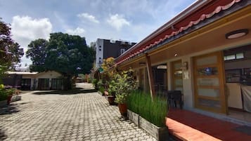 Un patio con sendero de baldosas, plantas en macetas y un edificio con tejado rojo y puertas de cristal.