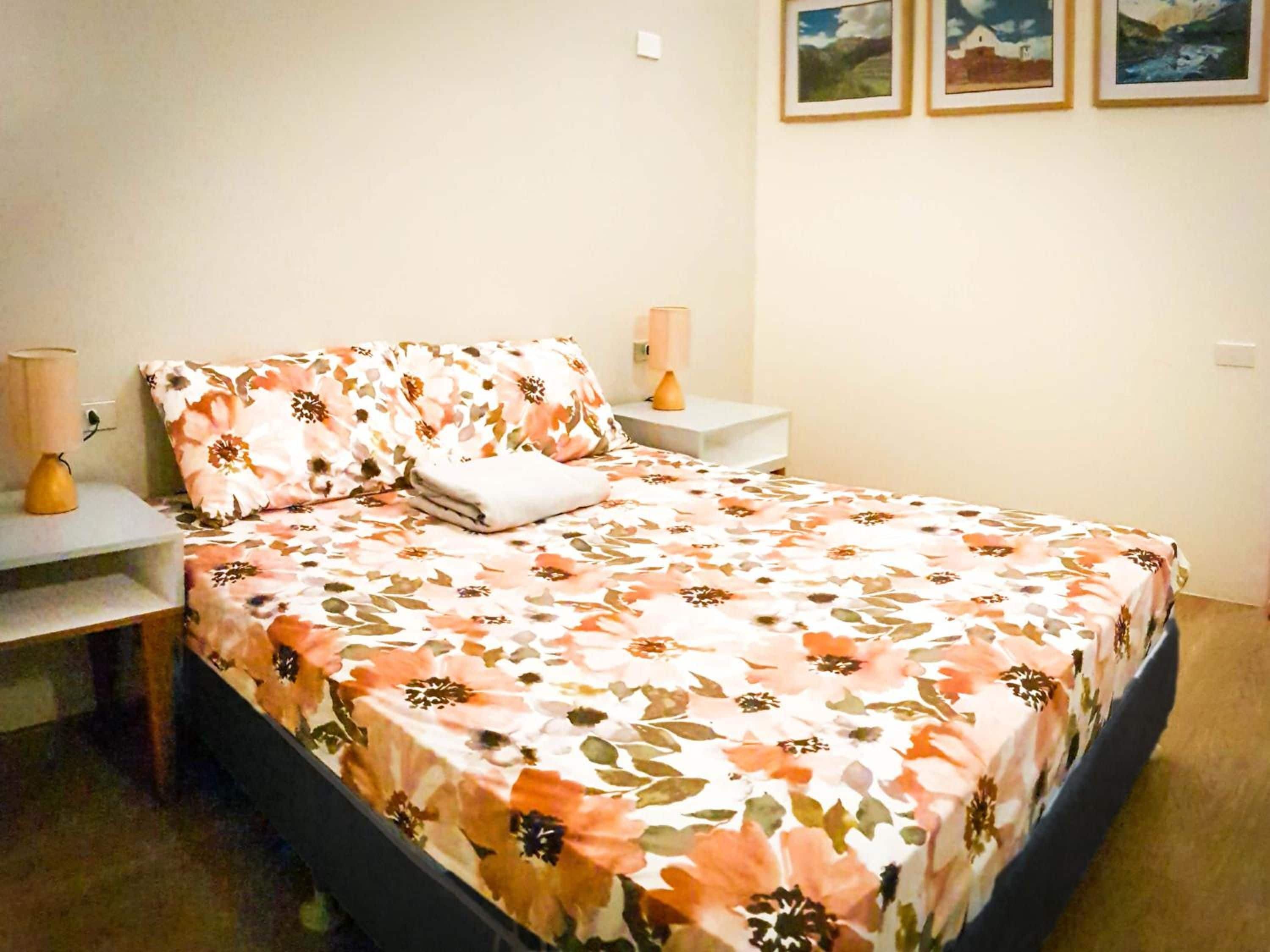 Una cama con colcha floral, una lámpara de noche y una mesita de noche con lámpara.