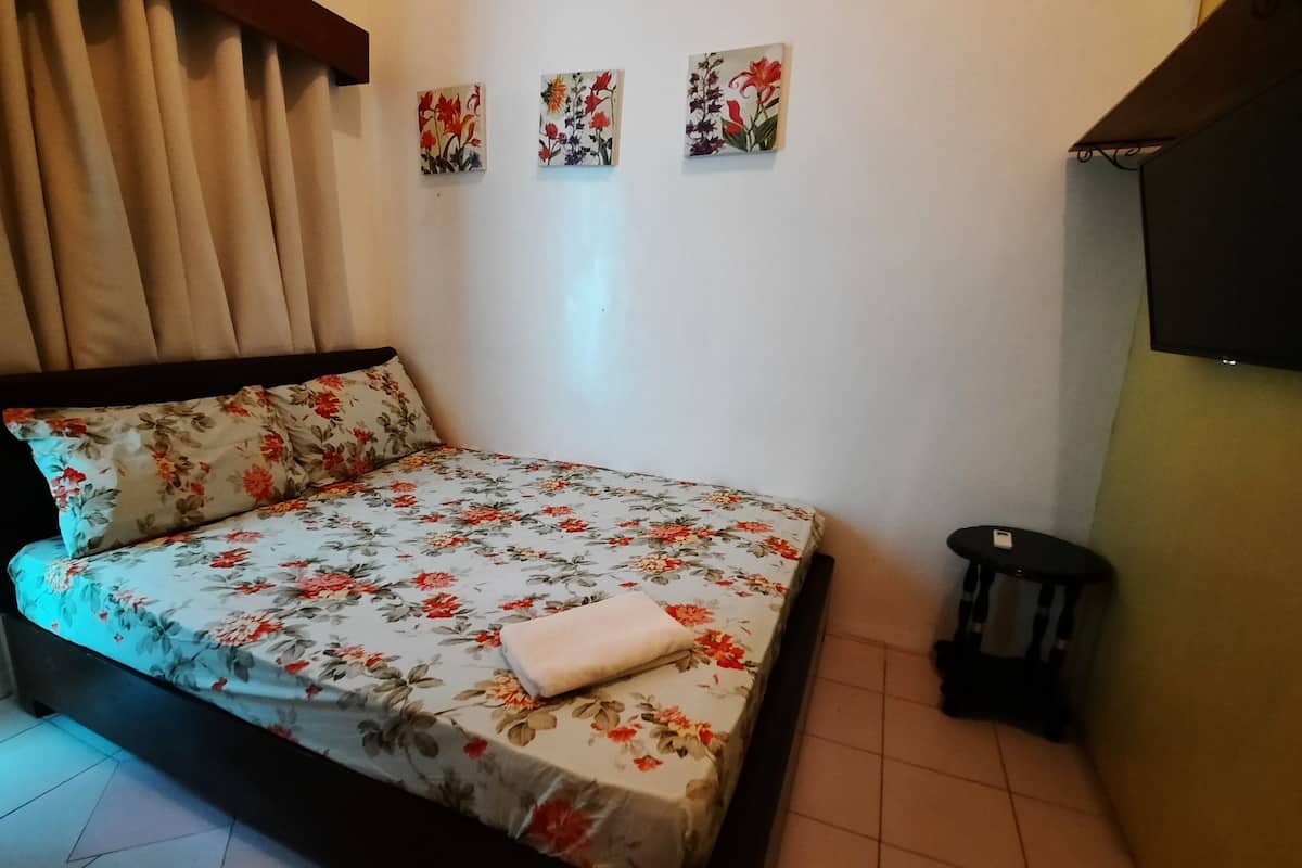 Uma cama com roupa de cama florida, uma mesinha de cabeceira, um pequeno banquinho e três quadros pendurados na parede.