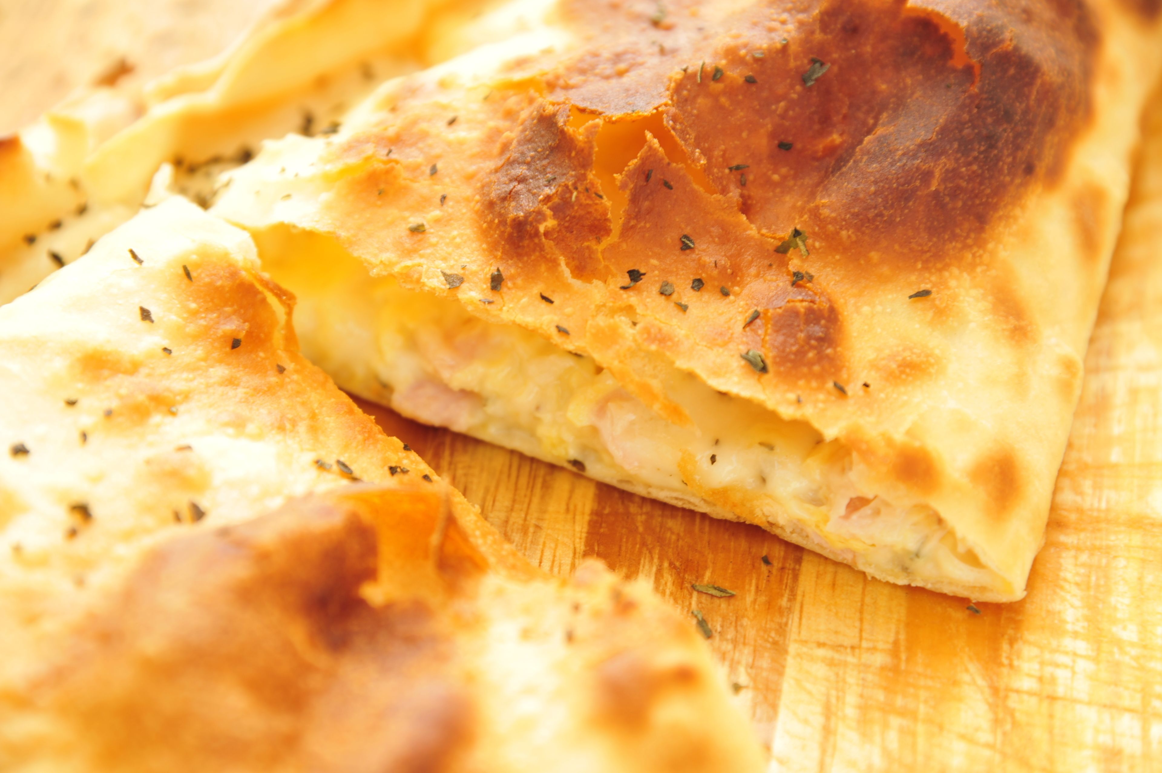 A close-up of a baked dish with a golden-brown crust, possibly a type of flatbread or pastry, on a wooden surface.