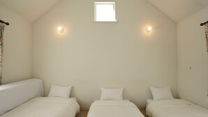 Une chambre avec deux lits simples, une petite fenêtre et deux lampes fixées au mur.