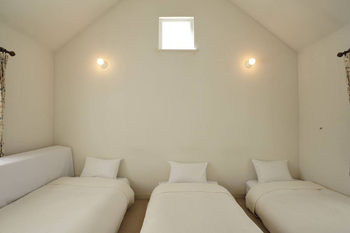 A room with two single beds, a small window, and two wall-mounted lights.
