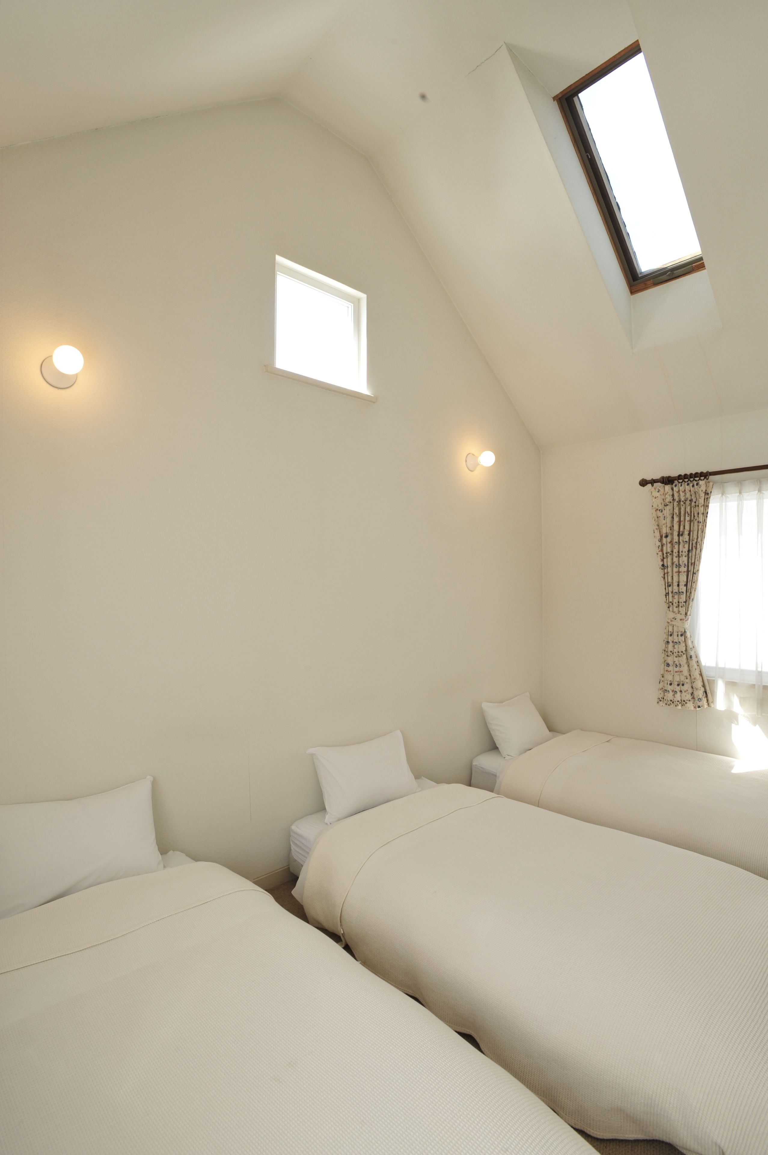 Une chambre avec deux lits, une lucarne et une petite fenêtre.
