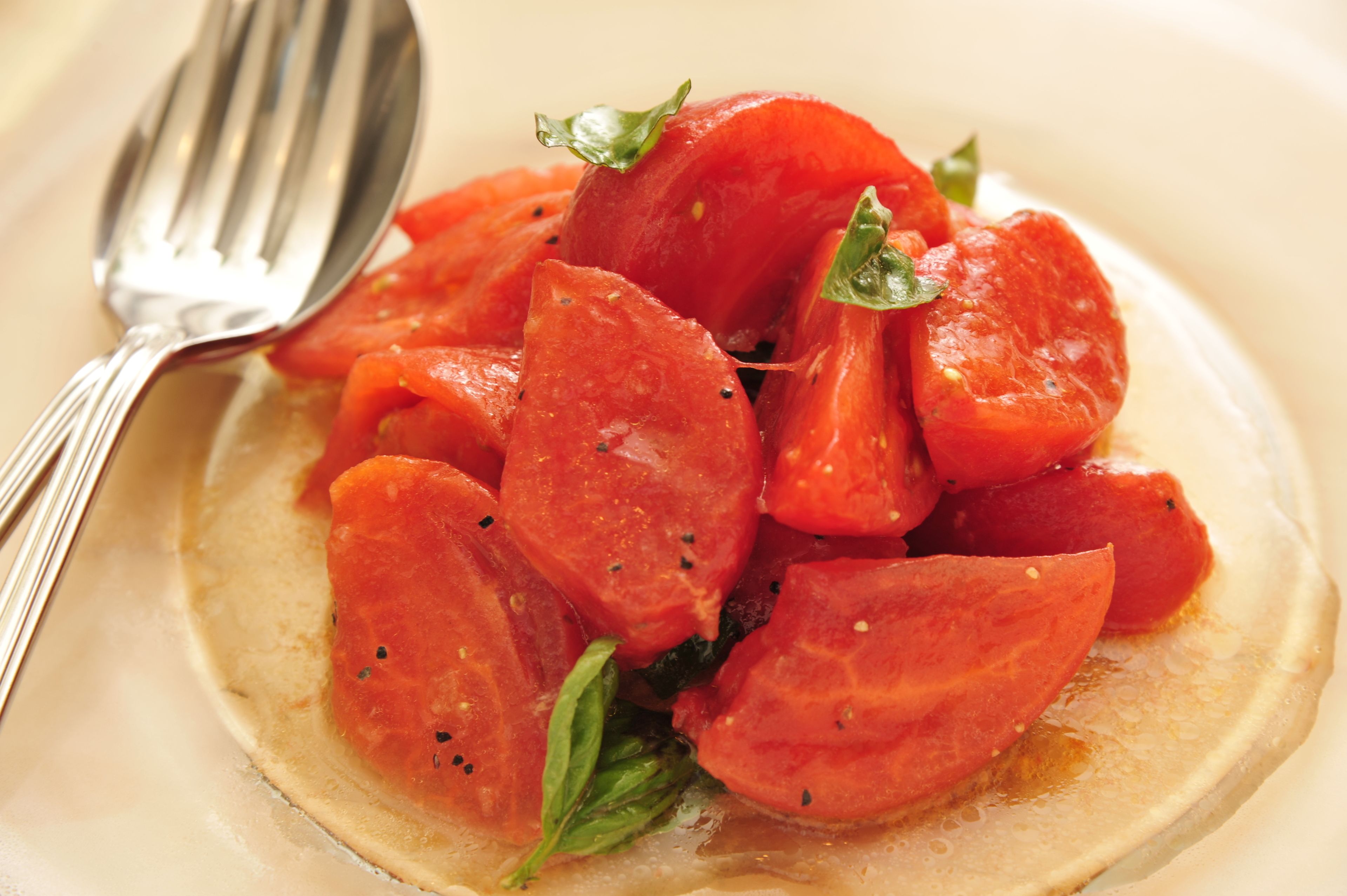 A plate of sliced tomatoes with basil, accompanied by a fork.