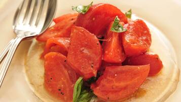 A plate of sliced tomatoes with basil, accompanied by a fork.