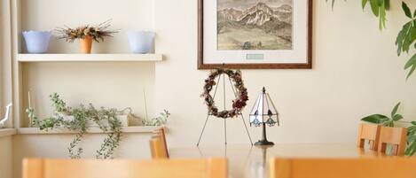 Uma área de refeições com cadeiras de madeira e uma mesa, decorada com uma grinalda, uma moldura com fotografia e uma planta pendente.