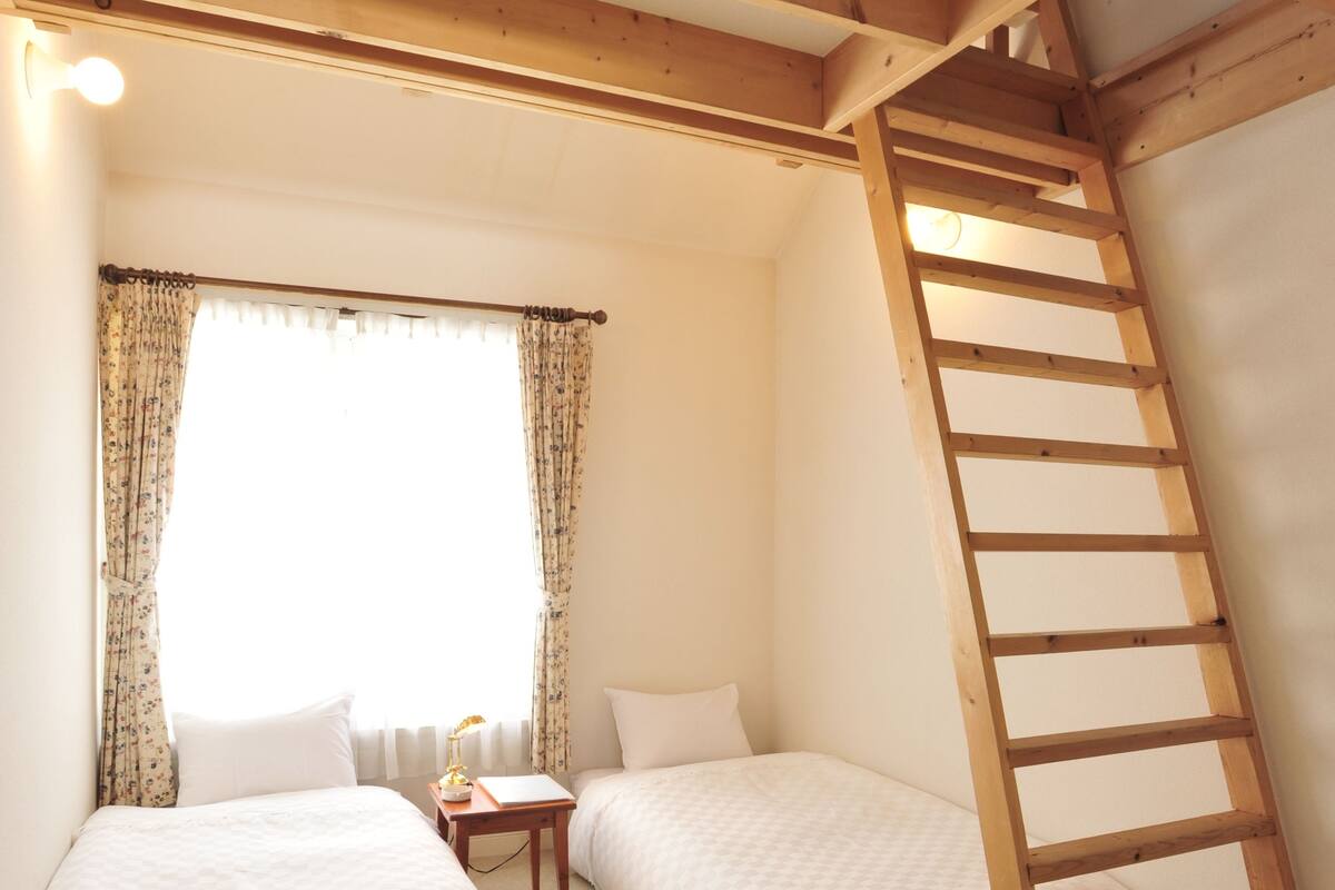 A small, cozy room with two beds, a wooden ladder, and a window with curtains.