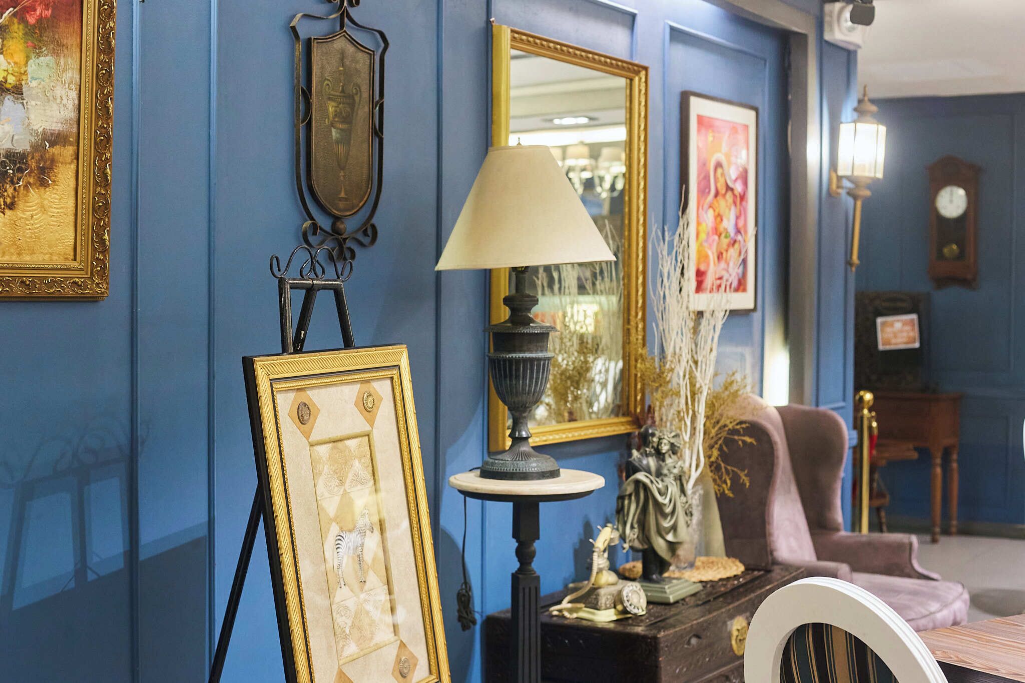 A room with blue walls, a lamp, framed pictures, and a statue.
