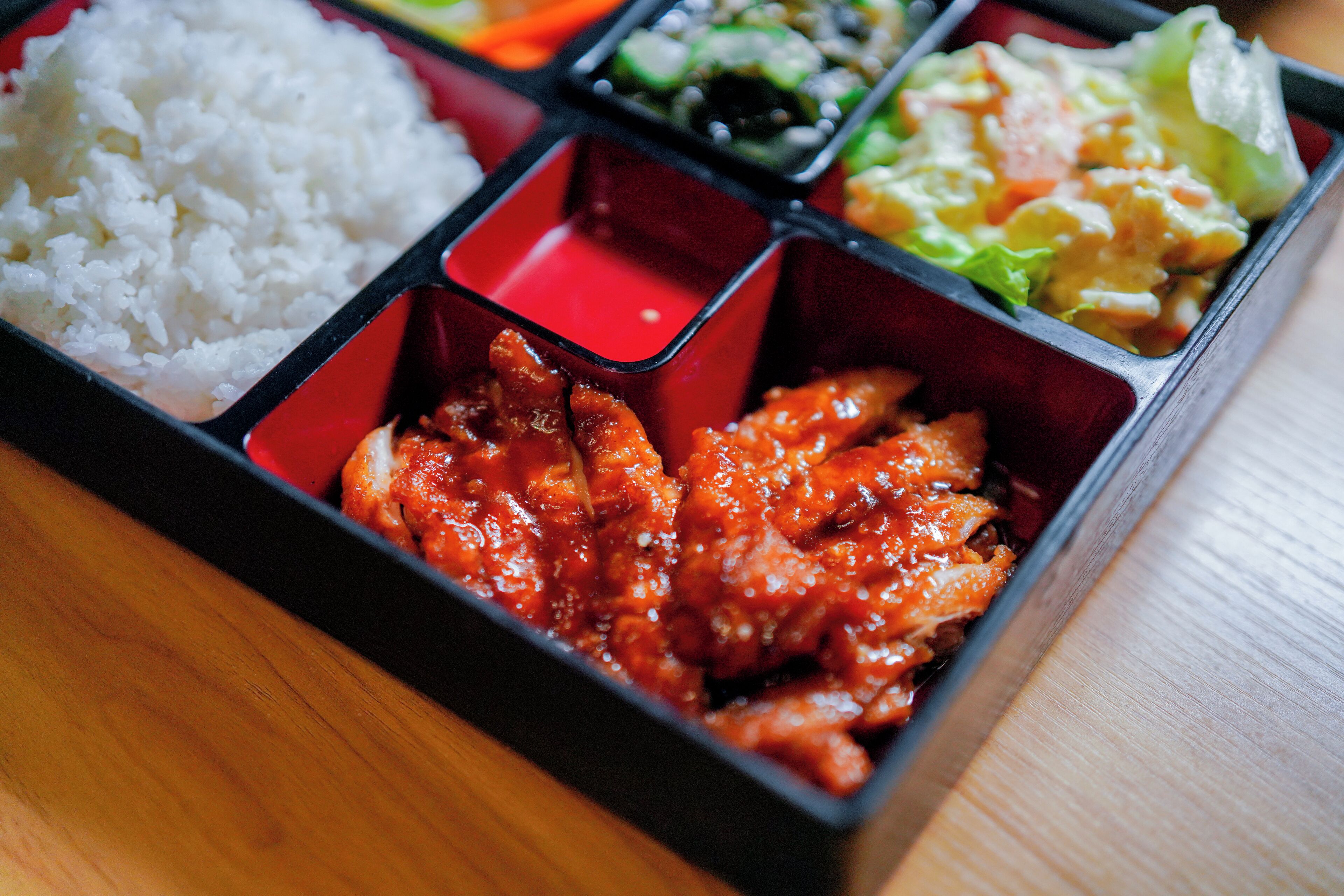A bento box with compartments containing rice, chicken, and vegetables.