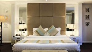 A hotel room with a large bed, two bedside tables with lamps, a mirror, and a chandelier.