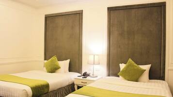A hotel room with two beds, each with a green accent pillow, a bedside table with a lamp, and a phone.