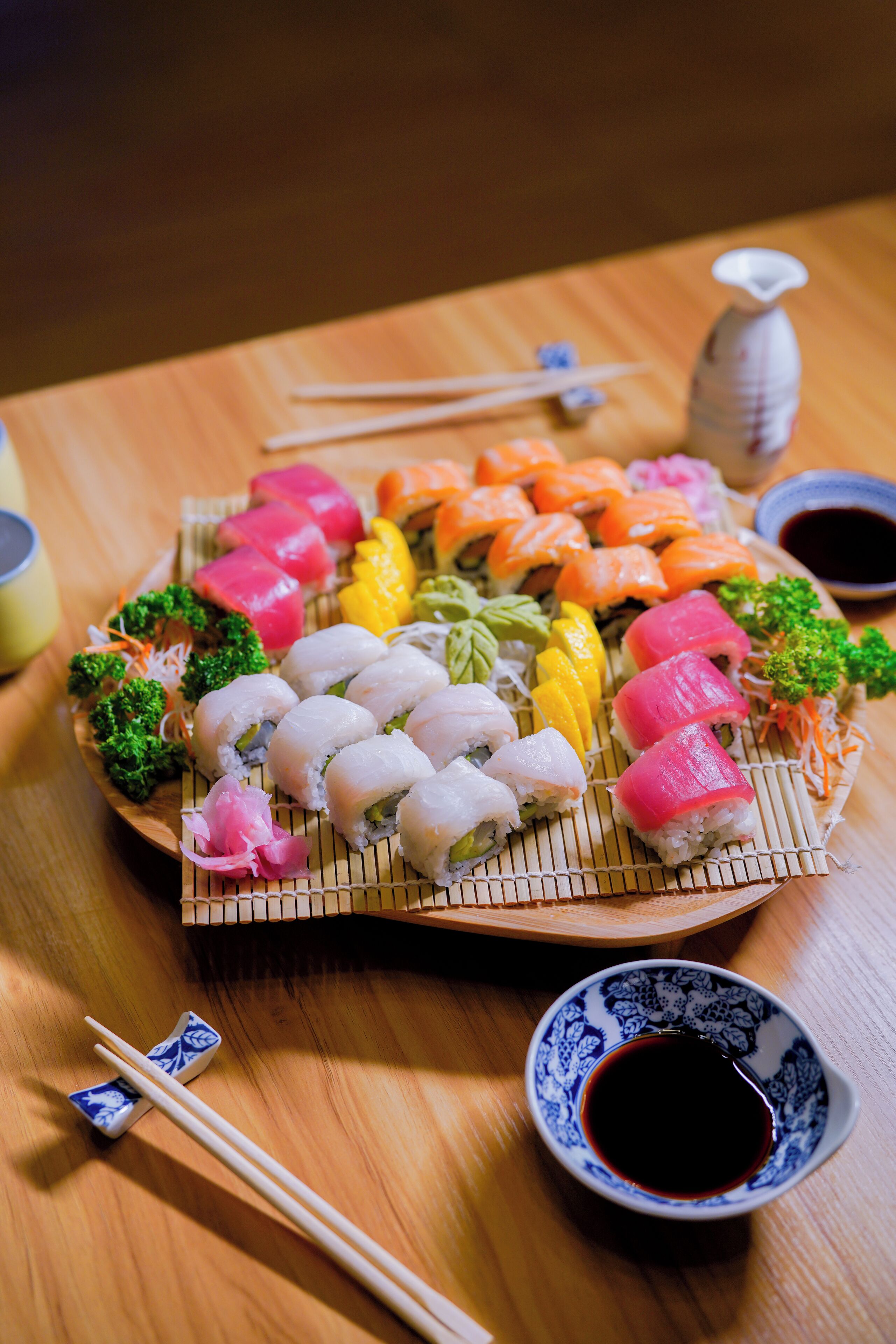 A sushi platter with various types of sushi, including nigiri and sashimi, arranged on a bamboo mat.