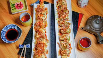 Two long dishes of food on rectangular plates, accompanied by small bowls of sauce and a teapot on a wooden table.