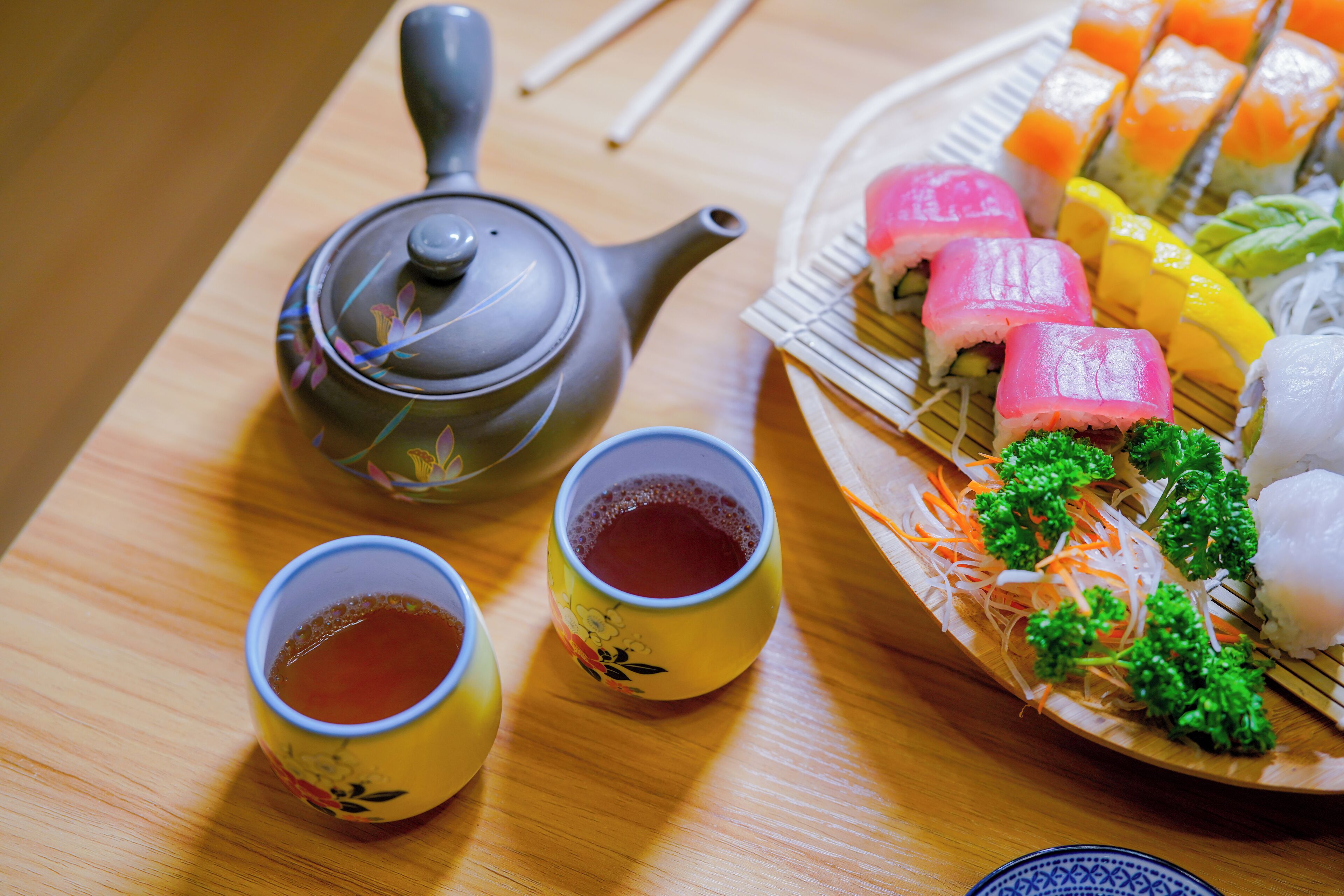 A table with a teapot, two cups of tea, and a plate of sushi.
