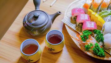 A table with a teapot, two cups of tea, and a plate of sushi.