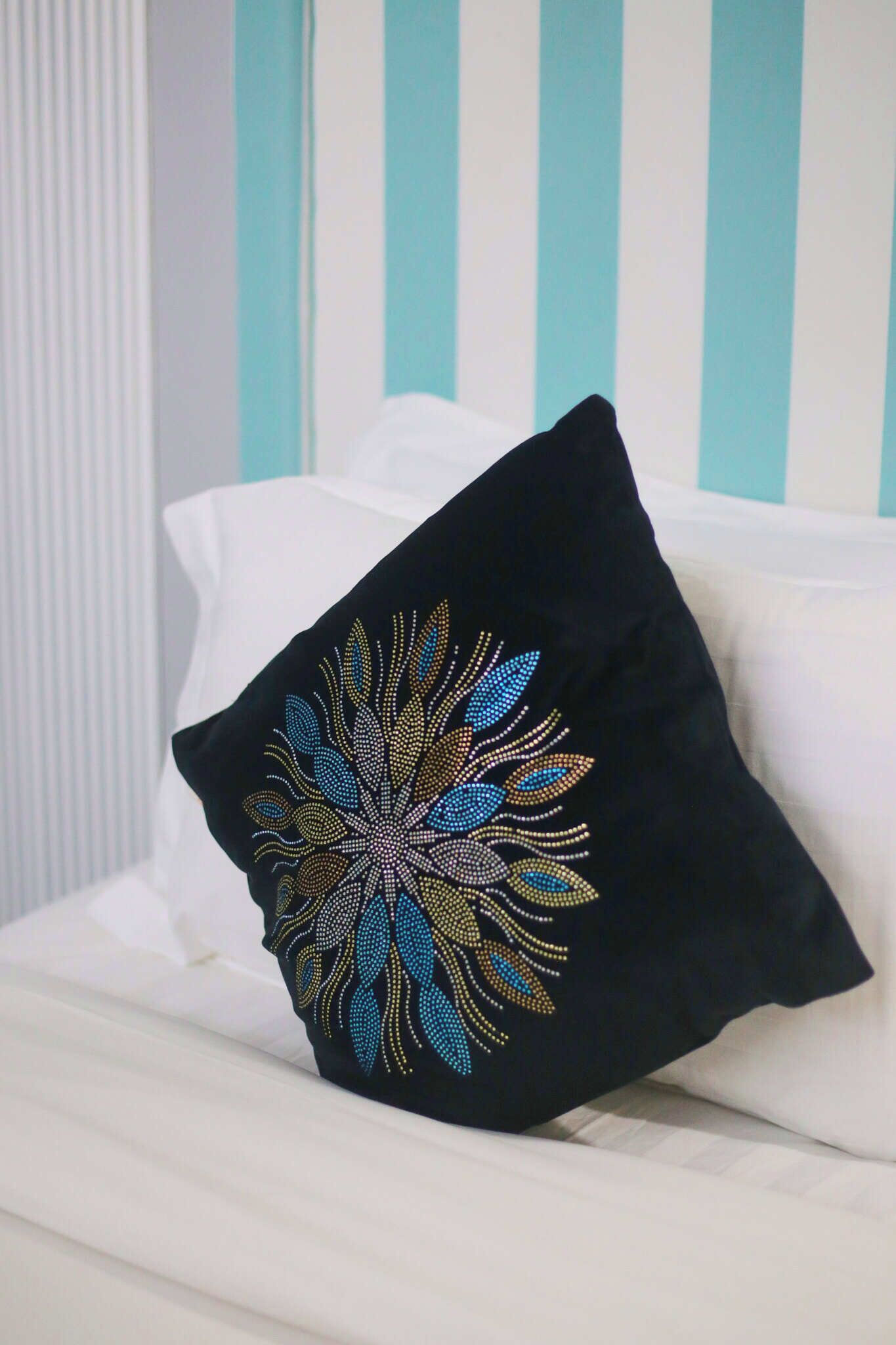 Un almohadón negro con un estampado floral colorido sobre un sofá blanco, frente a una pared a rayas.