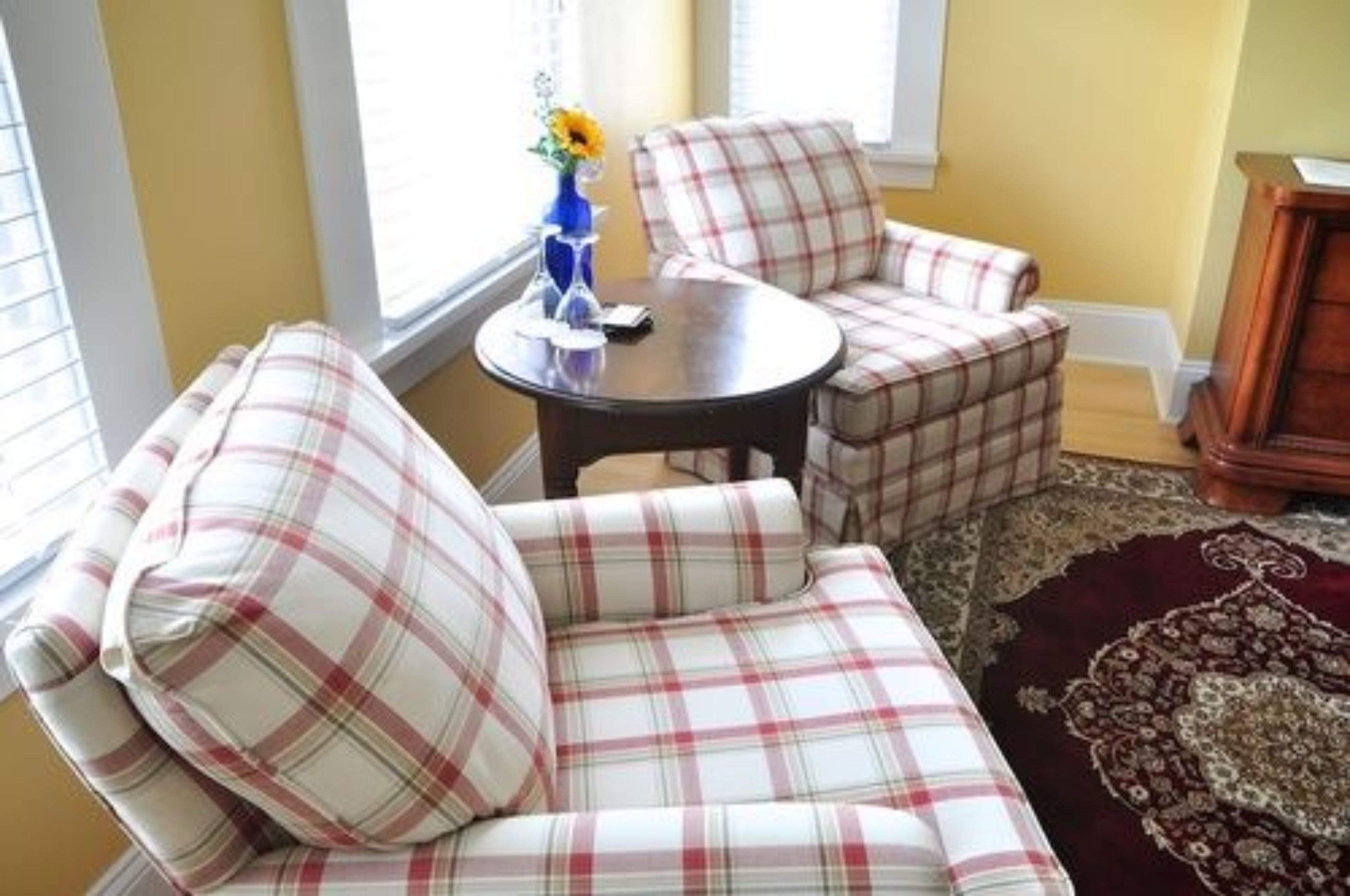 Un conjunto de sofá y sillón con estampado de cuadros en una habitación con una mesa de madera, un jarrón con flores y una alfombra estampada.