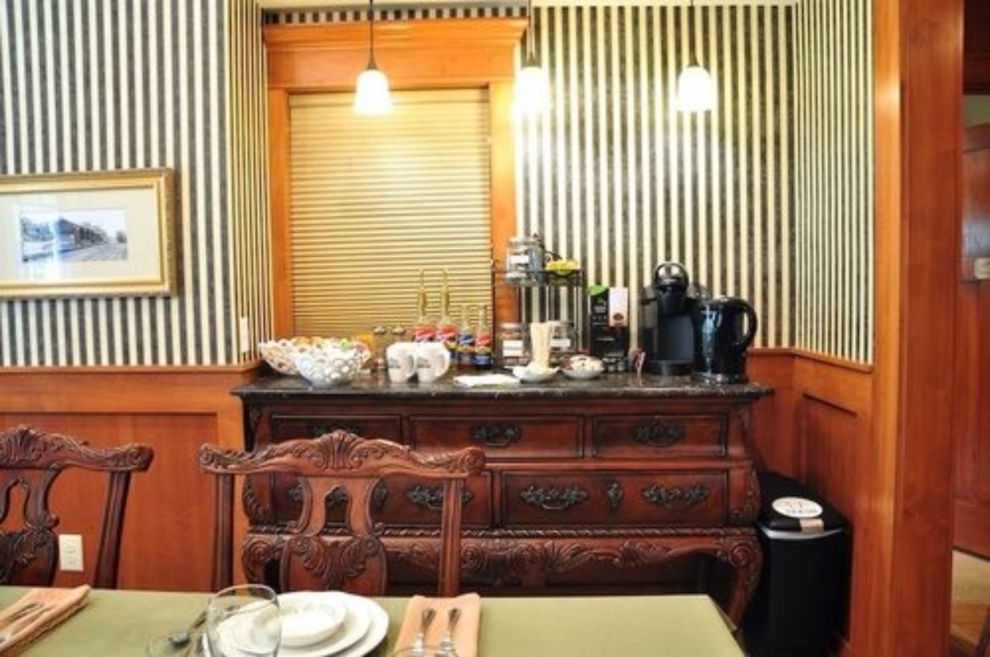 A dining area with a wooden buffet counter, framed picture, and a window with blinds.
